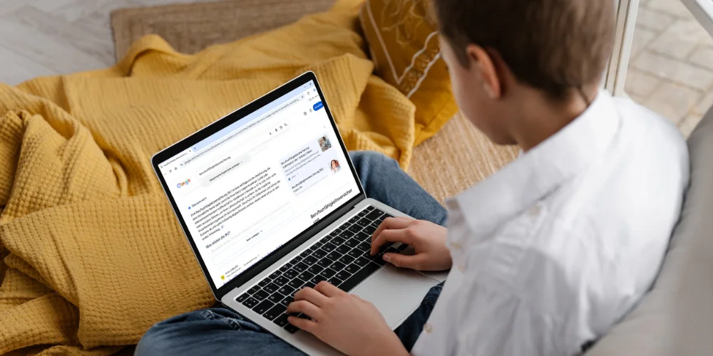 Mann sitzt auf einem Sofa mit Laptop und sieht bei der Suche nach ‚Berufsunfähigkeitsversicherung‘ eine direkte KI-Antwort im Google-Ergebnis.
